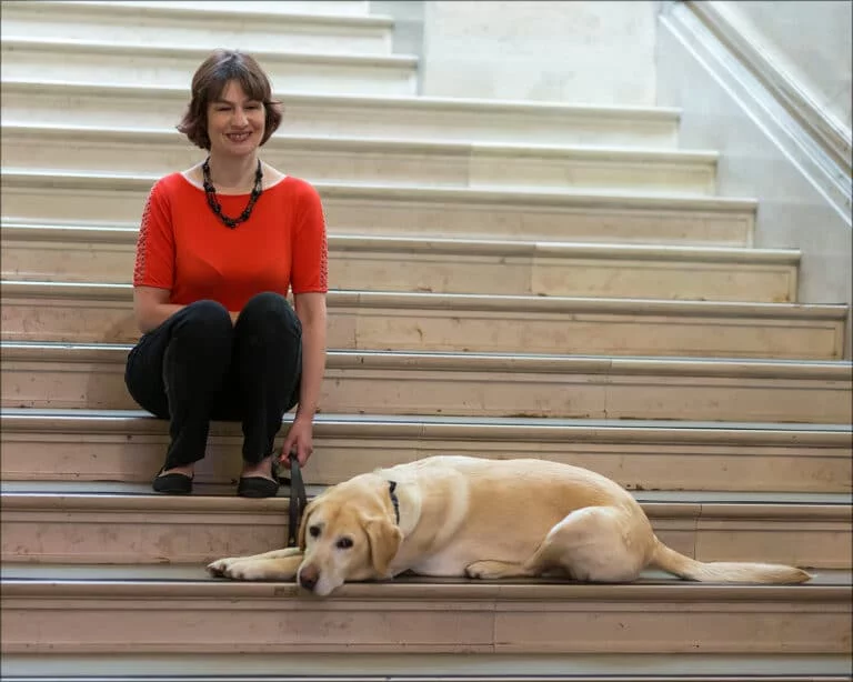 Nicki with guide dog sitting on stairs.